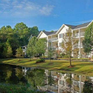 A serene apartment complex by a tranquil lake, surrounded by lush greenery.
