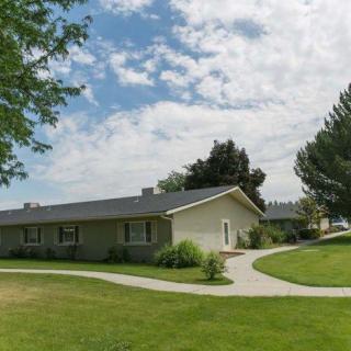 A single-story house surrounded by a well-maintained lawn with trees and a winding pathway under a partly cloudy sky.