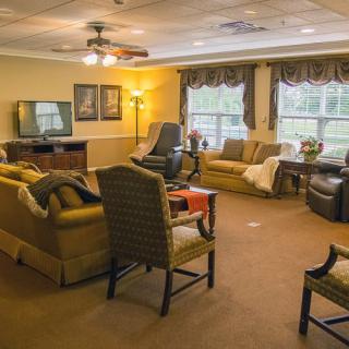 A cozy living room with sofas, chairs, and a TV, featuring large windows and warm lighting.