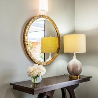 A beautifully styled entryway featuring a round mirror, a soft yellow lamp, and a floral arrangement on a console table.