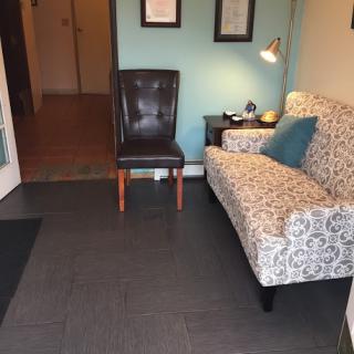 A cozy waiting room featuring a patterned sofa, a leather chair, and an end table with a lamp.