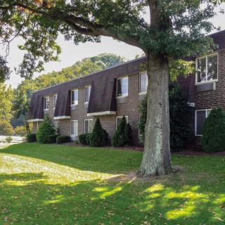 A suburban apartment building with a well-maintained lawn and large trees.