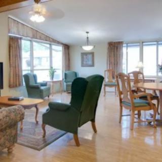 A spacious living and dining area featuring green armchairs, a wooden dining set, large windows, and hardwood flooring.