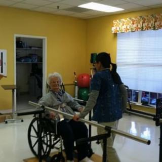 A healthcare worker assists an elderly person in a wheelchair during a physical therapy session.