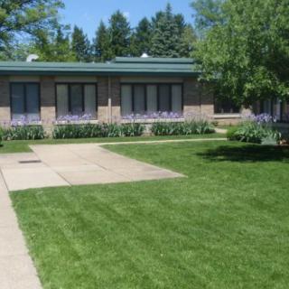 A view of a single-story building with large windows, surrounded by well-maintained grass and landscaping.