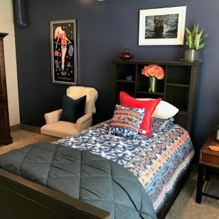 A cozy bedroom with a single bed, decorative pillows, and dark colored walls.