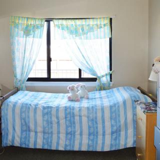 A neatly made bed with blue and white striped bedding, positioned next to a window with sheer curtains and a set of towels placed on top.