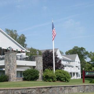 A building with an American flag on a flagpole, surrounded by trees and greenery under a clear blue sky.