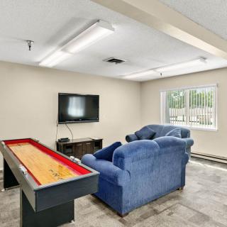 A cozy game room featuring a television, blue sofas, and a shuffleboard table.
