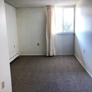 An empty room with a carpeted floor, white walls, and a window with curtains.