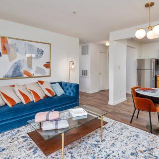 A modern living room and dining area with colorful decor, featuring a blue couch and abstract art.