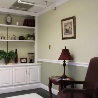 A cozy office space featuring a green wall, shelves filled with decor, and a comfortable chair.