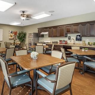 A community dining area with several tables and chairs, featuring a kitchen with wooden cabinets in the background.