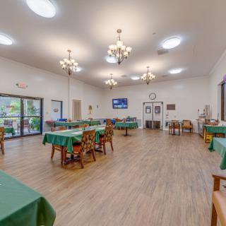 A spacious dining room featuring several tables and chairs, illuminated by chandeliers, with large windows providing natural light.