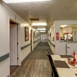 A well-lit hallway in a care facility, featuring doors leading to individual rooms and a dining area.