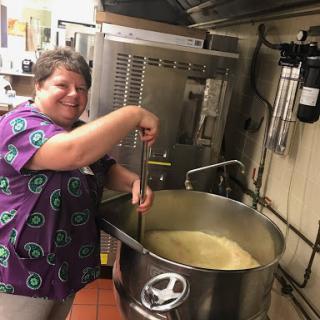 A woman happily stirring a large pot of soup in the kitchen.