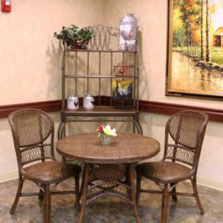 A cozy indoor corner featuring a rattan table and chairs with decorative shelving and artwork.