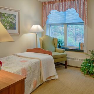 A cozy bedroom with a single bed, armchair, and a large window allowing natural light to fill the room.