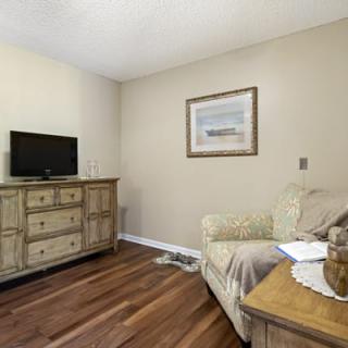 A cozy living room with a small TV on a wooden dresser, a couch, and a framed picture on the wall.