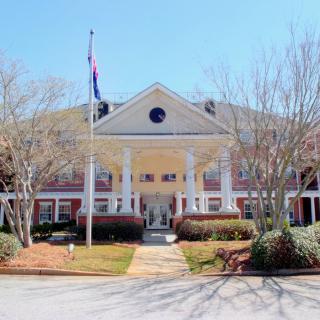 A grand building entrance with large columns and a flagpole, surrounded by landscaped greenery.