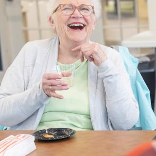 An elderly woman laughing while enjoying a meal indoors.