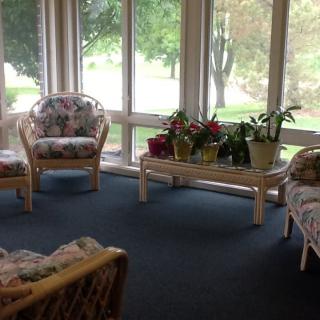 A cozy sunroom with wicker furniture and potted plants, surrounded by large windows.