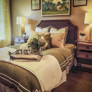 A cozy and elegantly decorated bedroom with a neatly made bed, decorative pillows, bedside lamps, and framed artwork on the wall.