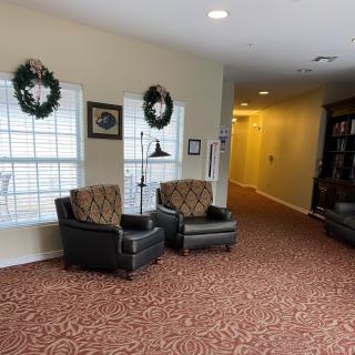 A cozy lobby area with patterned carpet, two armchairs, and holiday wreaths on the windows.