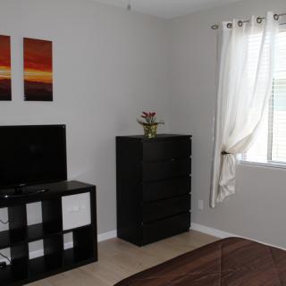 A minimalist bedroom with a dresser, television, and window with curtains.