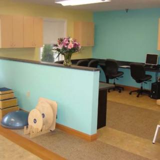 A reception area with a desk, chairs, and exercise equipment against a turquoise wall.