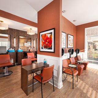 A modern salon interior featuring a waiting area with orange chairs, hair dryers, and vibrant artwork on the walls.