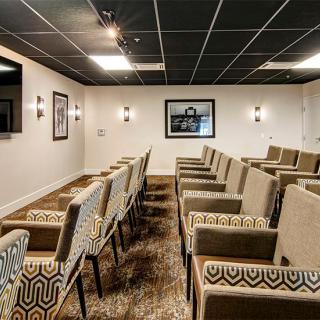 A small conference room with neatly arranged chairs facing a projector screen, accompanied by ambient lighting and wall dcor.