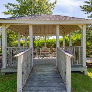 A wooden gazebo in a garden setting with surrounding greenery and outdoor seating.