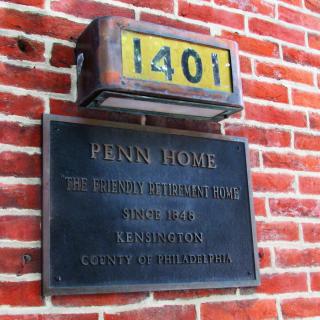 A building plaque and house number on a brick wall displaying 'Penn Home' and address details.