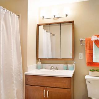 A clean and organized bathroom with a wooden cabinet, mirror, and modern fixtures.