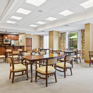 A spacious dining area with neatly arranged tables and chairs, featuring a kitchenette and large windows.