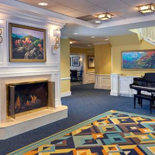 A cozy lobby area featuring a lit fireplace, artwork on the walls, and a grand piano.