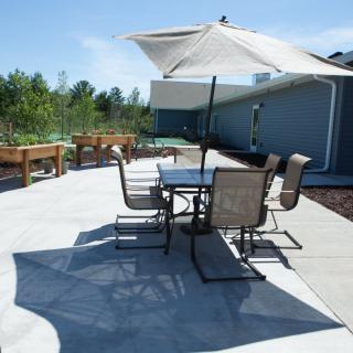 A sunny outdoor patio with a table, chairs, and an umbrella.