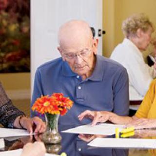 A group of elderly individuals engaged in reading and discussion at a table.
