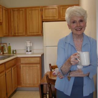 A smiling woman stands in a kitchen holding a coffee cup.