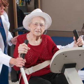 An elderly woman receiving assistance while exercising on gym equipment.