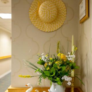 A cozy hallway corner featuring a straw hat on the wall, a vibrant flower arrangement in a vase, and a candlestick.