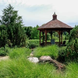 A serene garden featuring a wooden gazebo surrounded by lush greenery and trees.