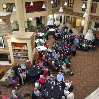 A large group of people seated at round tables in a spacious indoor setting, possibly attending a social event or meeting.
