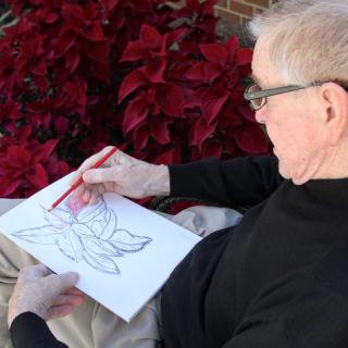 A person sketching a flower while sitting outdoors.