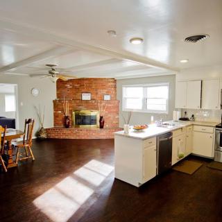 A cozy open space featuring a kitchen and dining area with a brick fireplace and hardwood flooring.