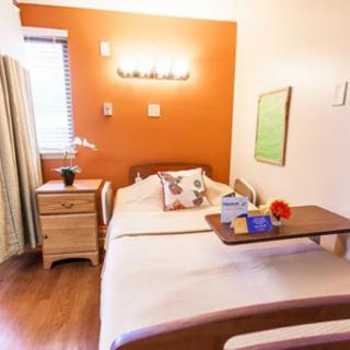 A cozy hospital room with a single bed, orange accent wall, and a bedside tray table.