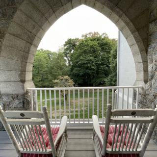 A pair of rocking chairs on a balcony with a scenic view through an arched stone structure.