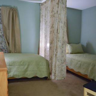 A cozy bedroom with twin beds adorned in green bedding, separated by floral curtains.