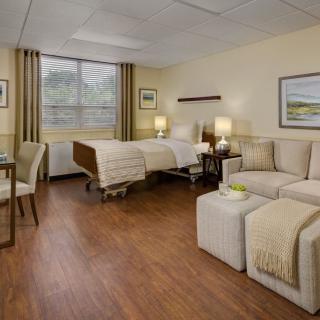 A comfortable hospital room featuring a bed, sofa, and wooden flooring.